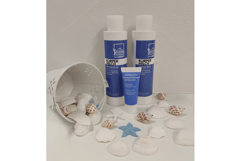 Drei Tuben Körpermilch 'After Sun' vor einem Eimer mit Muscheln und einem blauen Seestern auf weißem Hintergrund.