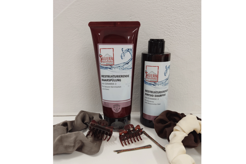 Zwei Flaschen Haarpflegeprodukte in einer roten Verpackung und Haarschmuck wie Haargummis und Klammern auf einem Tisch.