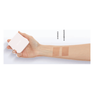 Eine Hand hält einen quadratischen, weißen Verpackung mit zwei bronzefarbenen Farbstrichen auf dem Arm.