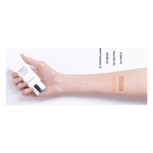 Eine Hand hält eine Tube Flüssigfoundation, daneben sind vier Farbstriche auf dem Unterarm abgebildet.