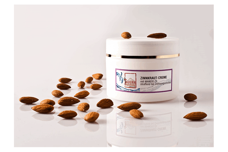 Weiße Zinkraut-Creme mit Mandelöl in einem runden Behälter, umgeben von Mandeln auf einem weißen Hintergrund.