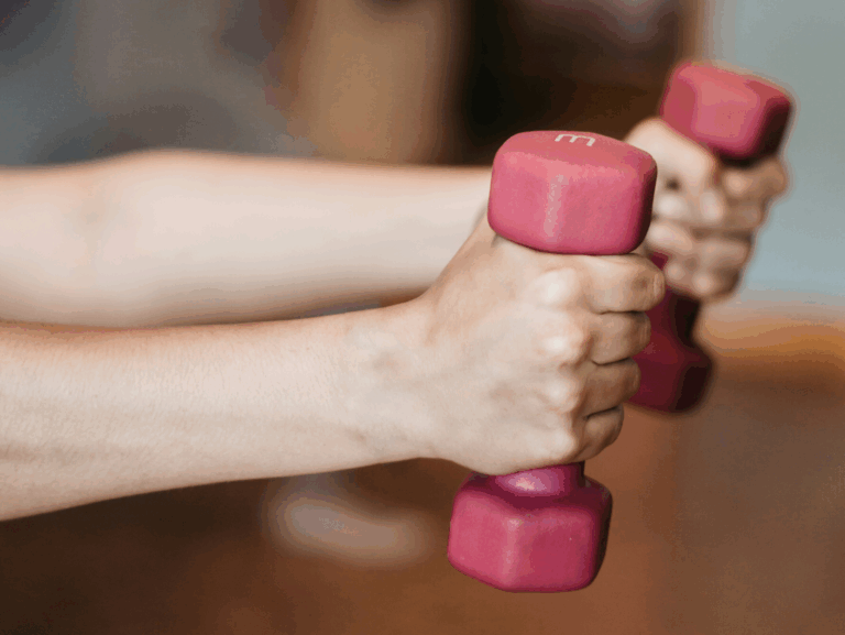 Hände halten zwei pinkfarbene Kurzhanteln in einem Fitnessstudio.