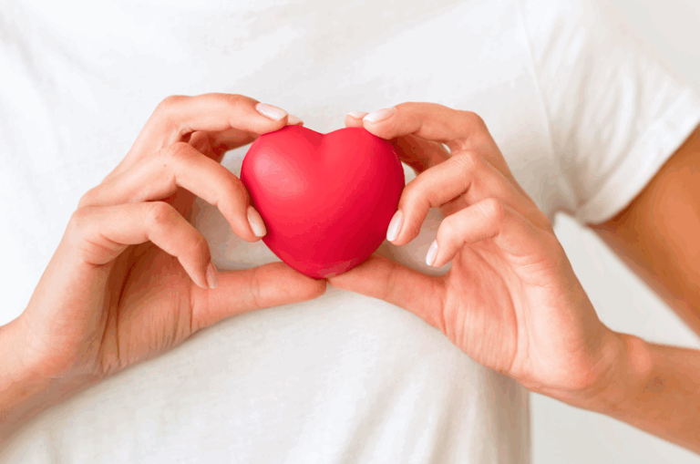 Eine Person hält ein rotes Herzen in beiden Händen vor einem hellen Hintergrund.