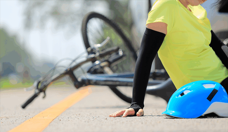 Eine Person in einem gelben Shirt sitzt auf der Straße neben einem blauen Fahrradhelm und einem umgekippten Fahrrad.