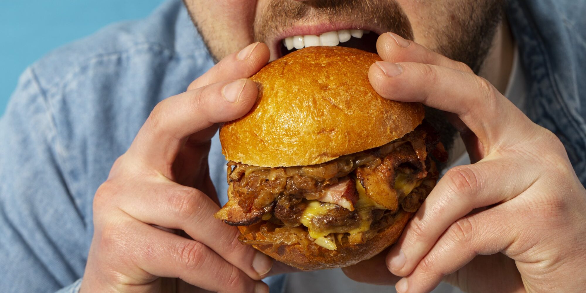 Tierische_Fette__1_.jpg Eine Person hält einen saftigen Burger mit einem goldenen Brötchen und beabsichtigt, ihn zu essen.