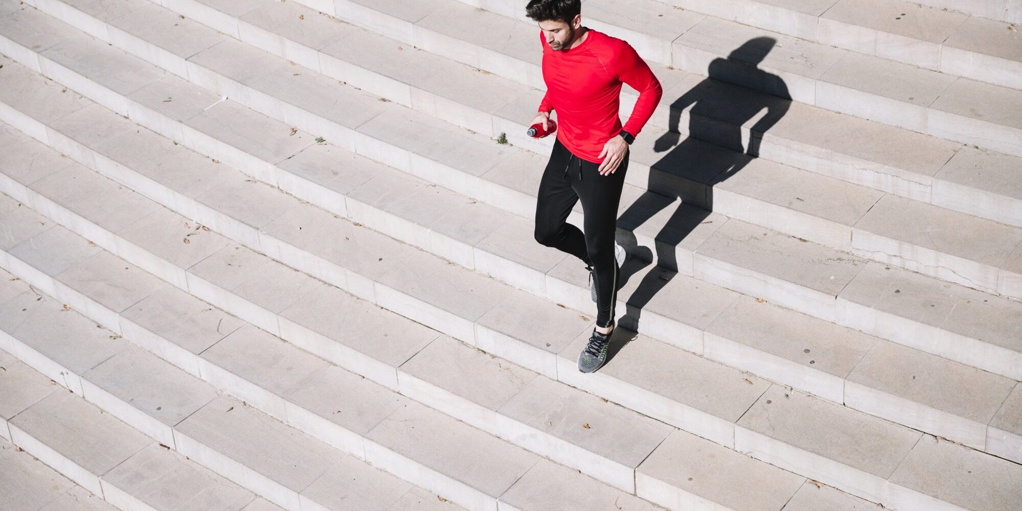 Mann in rotem Shirt joggt über eine helle Treppe, sein Schatten ist deutlich sichtbar.