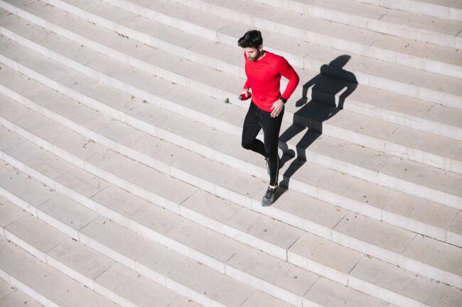 Stiegensteigen_Fitness.jpg Mann in rotem Shirt joggt über eine helle Treppe, sein Schatten ist deutlich sichtbar.