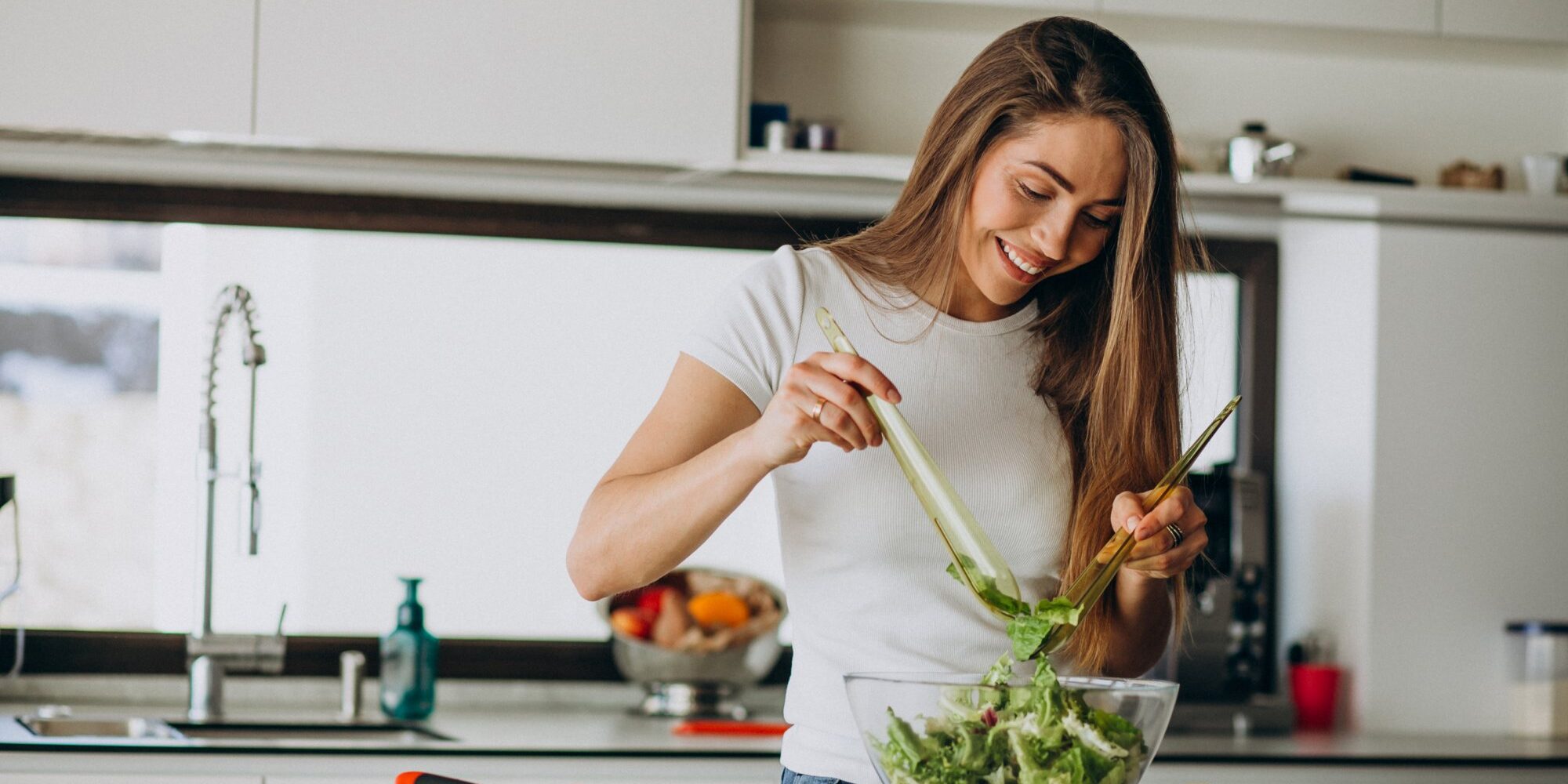 ernaehrung.jpg Frau mischt Salat in einer Schüssel in einer modernen Küche, umgeben von frischen Zutaten.