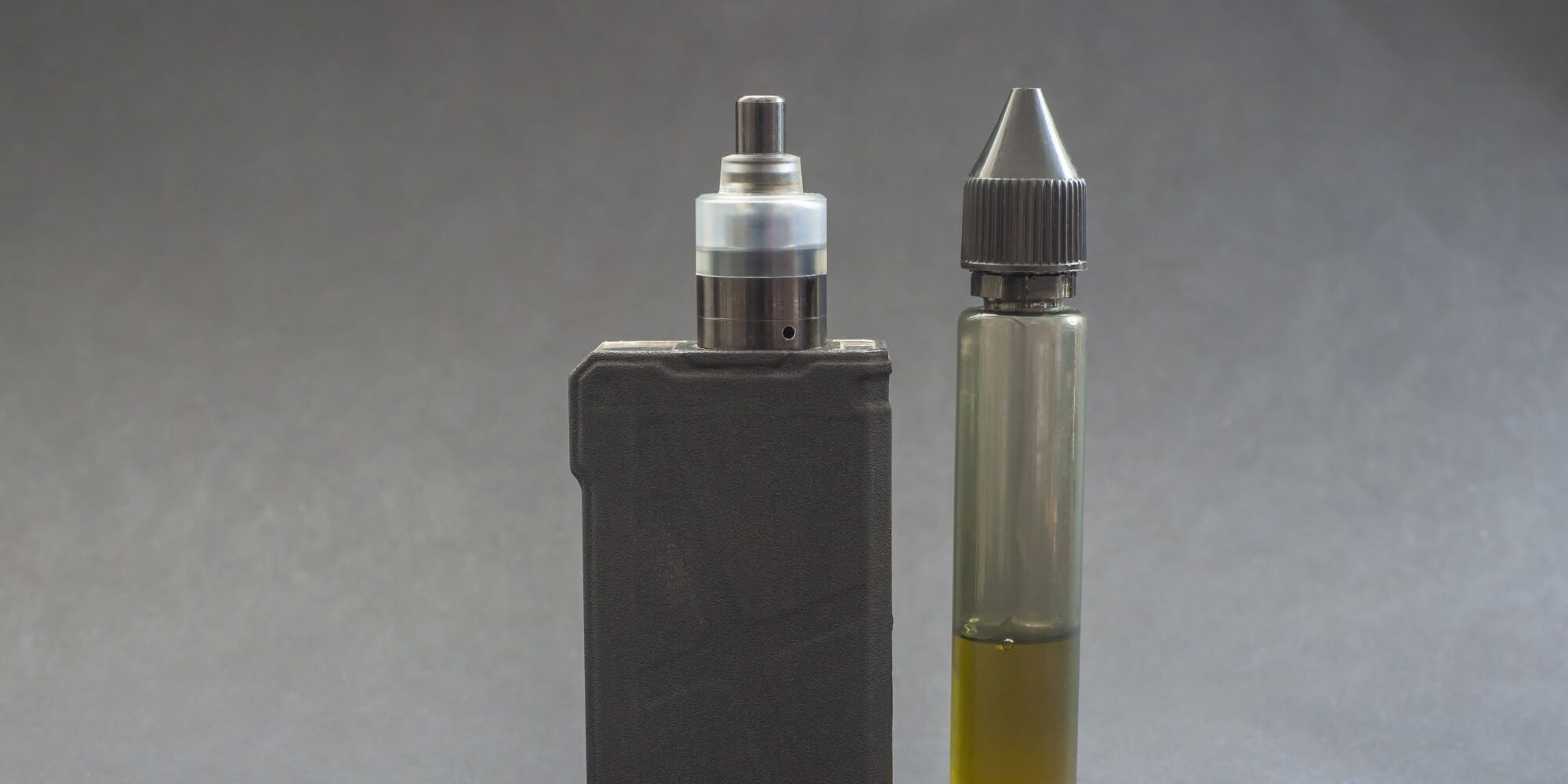 e-zigarette.jpg Ein Verdampfergerät links, daneben eine Flasche mit E-Liquid in einer transparenten Verpackung.