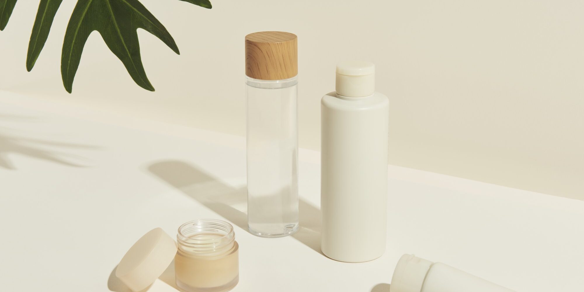 Verschiedene kosmetische Flaschen und Tiegel, darunter ein Glas mit Holzstoß, auf einem hellen Untergrund.