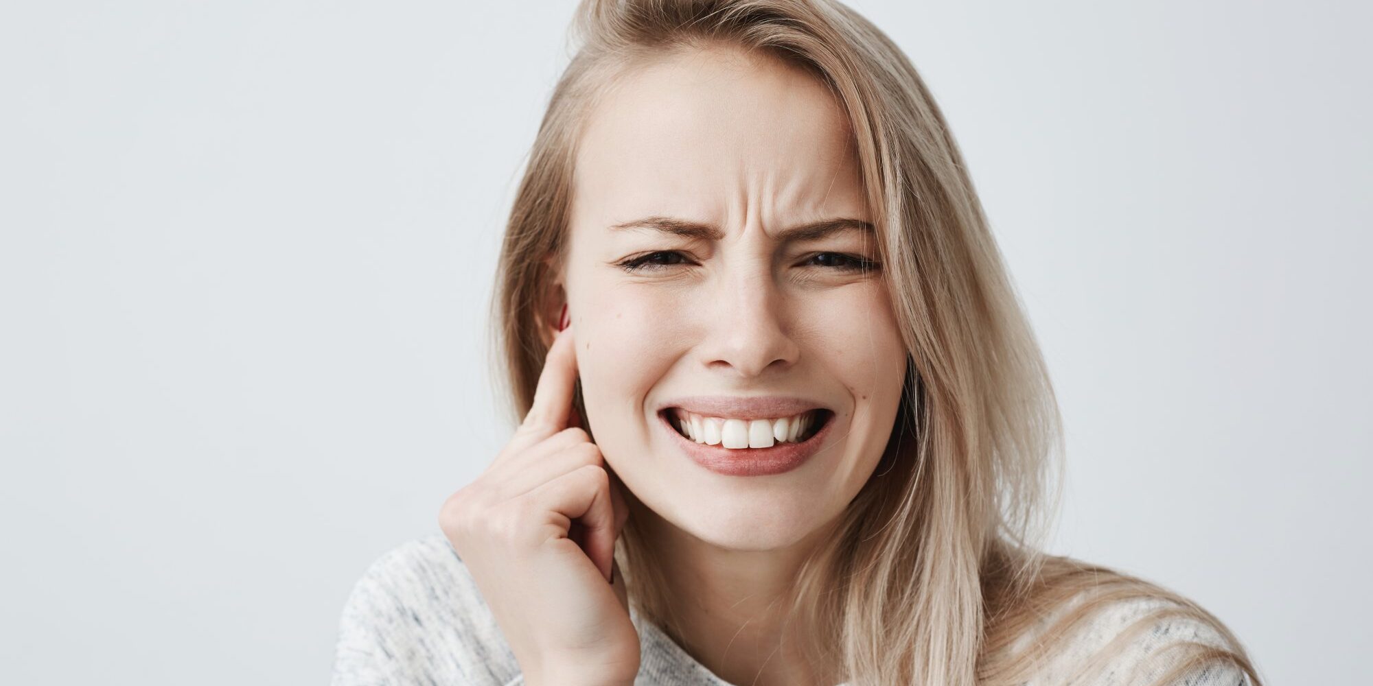 Junge Frau mit schmerzverzerrtem Gesicht, hält sich den rechten Ohrbereich mit der Hand.