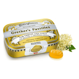 Gelbe Dose mit Grether's Pastillen für Hals und Stimme, umgeben von Holunderblüten.