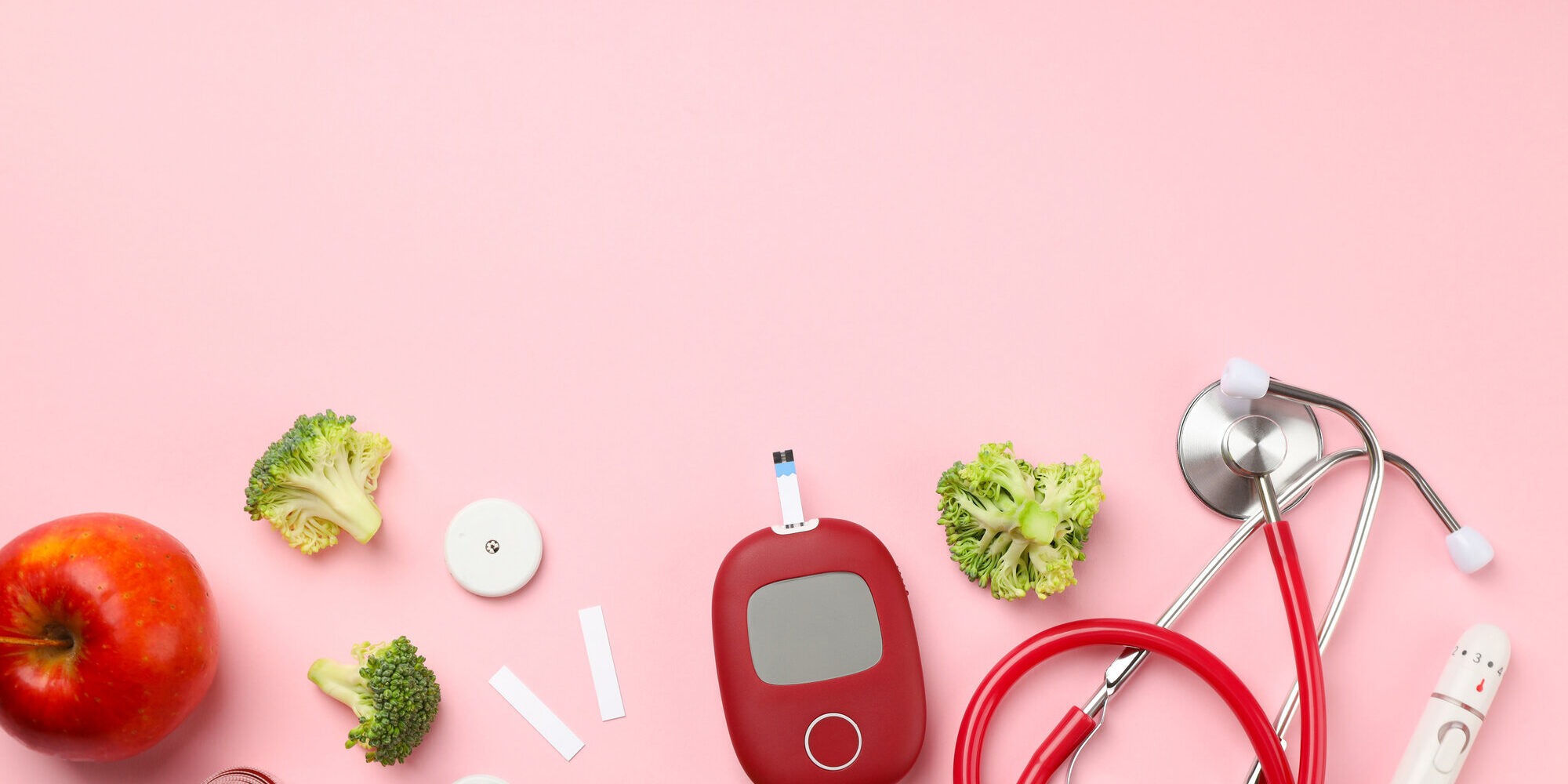 Blutzucker-spitzen.jpeg Gesunde Lebensmittel und medizinische Geräte auf rosa Hintergrund, darunter Apfel, Brokkoli, Blutzuckermessgerät und Stethoskop.