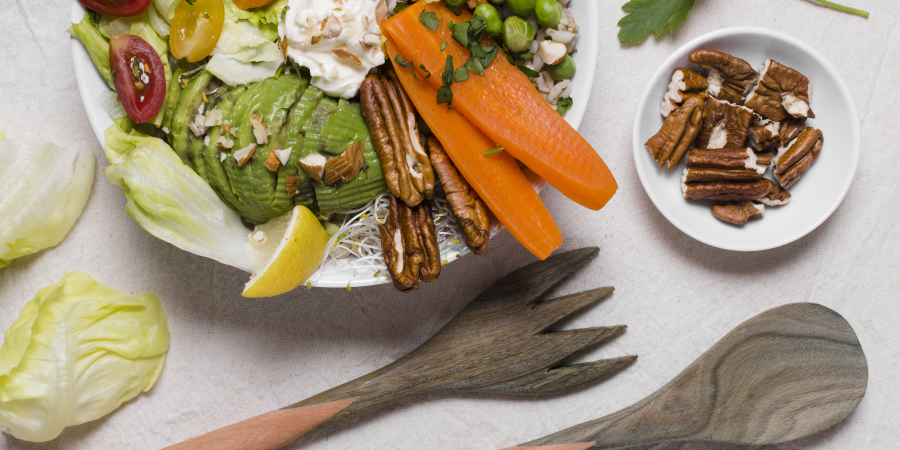 Bunte Salatschüssel mit Avocado, Karotten, Erbsen, Mais, Tomaten und Nüssen, begleitet von Holzbesteck und einer Schale Nüssen.
