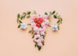 Ein florales Arrangement in Herzform aus rosa Blumen und Baumwollblüten auf einem pfirsichfarbenen Hintergrund.